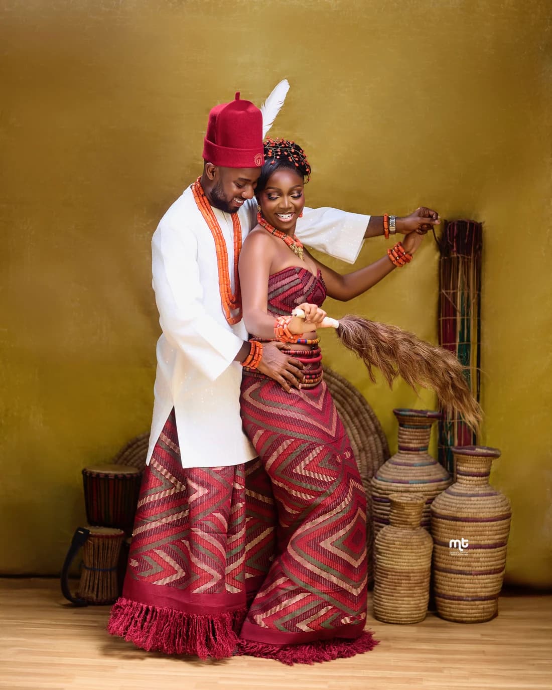 Mimi and Dalu in traditional Igbo wedding attire, red coral beads and George wrappers, holding an isiala horsetail whisk